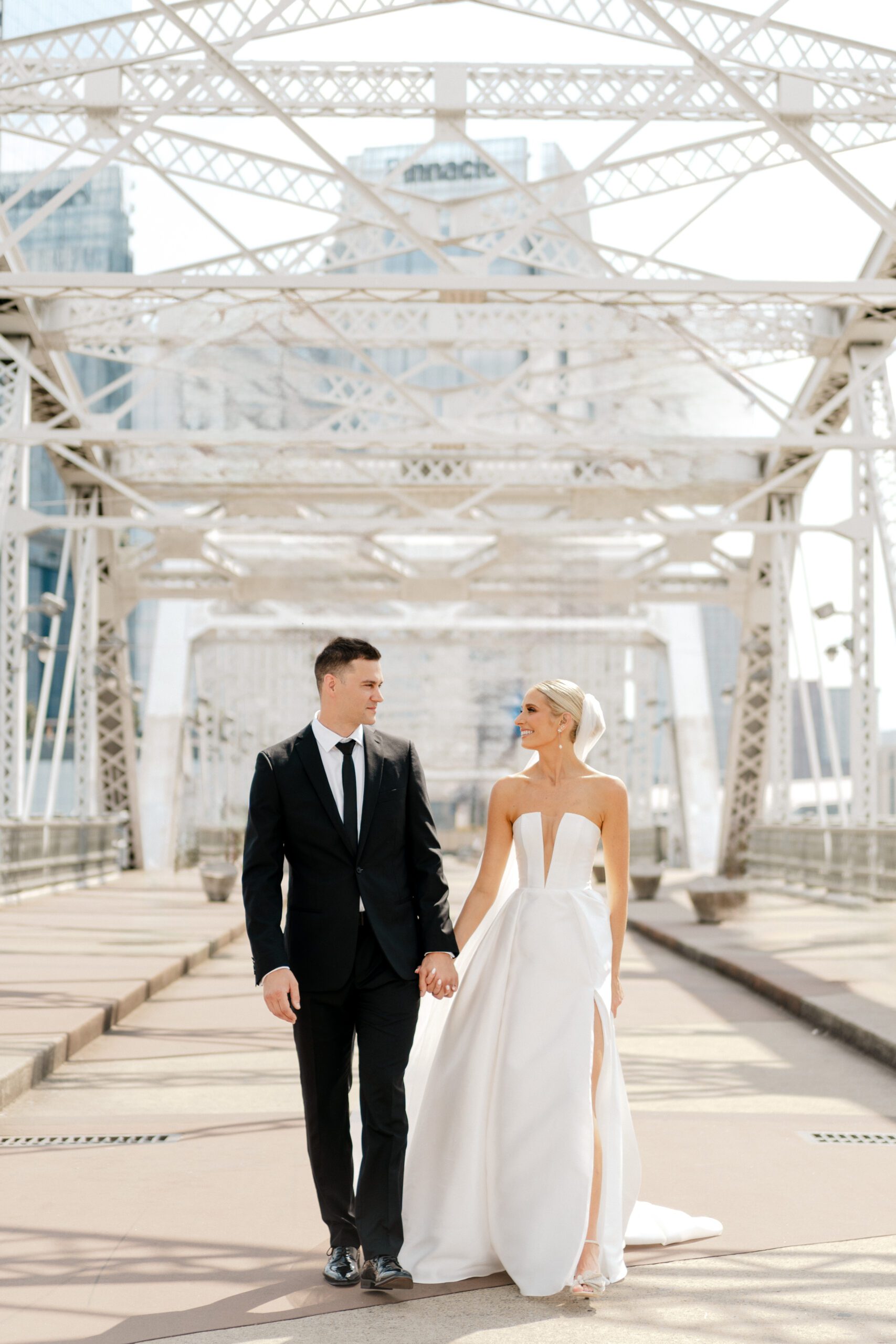 couple holding hands while walking on the pedestrian bridge in downtown nashville before their wedding
