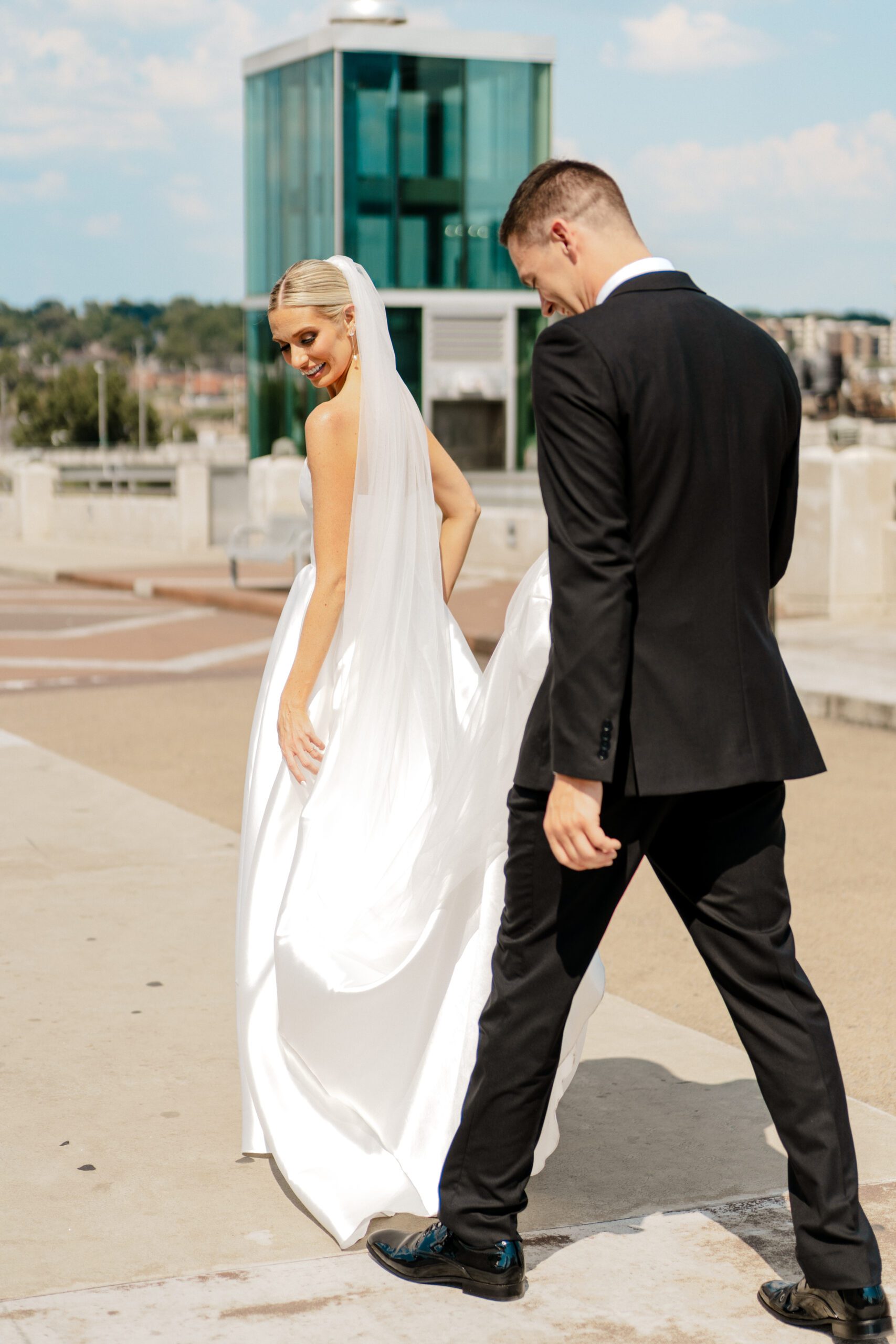 groom holding brides dress while walking back into the bridge building in downtown nashville