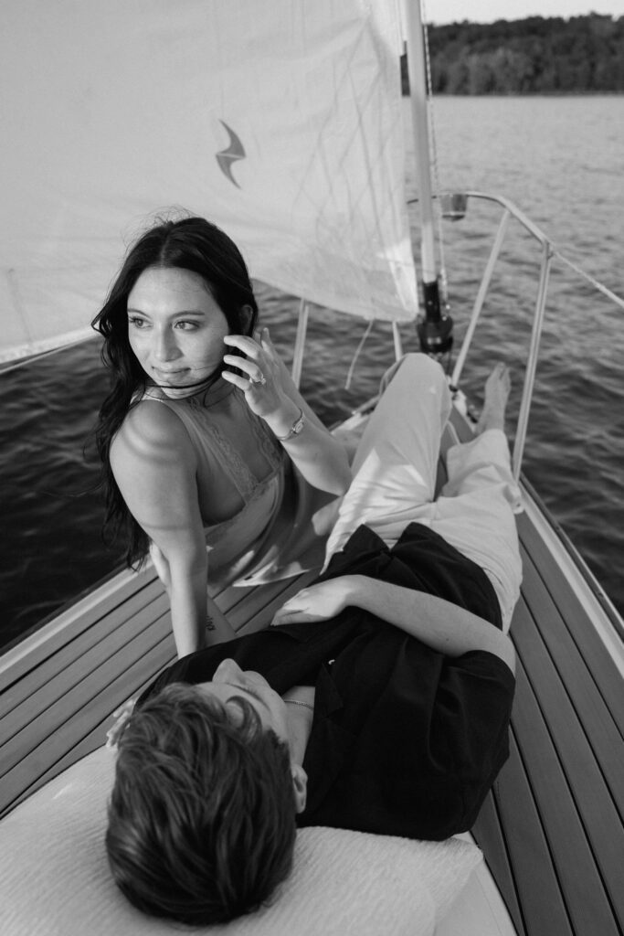 black and white image of couple sitting at the front of the sailboat during golden hour
