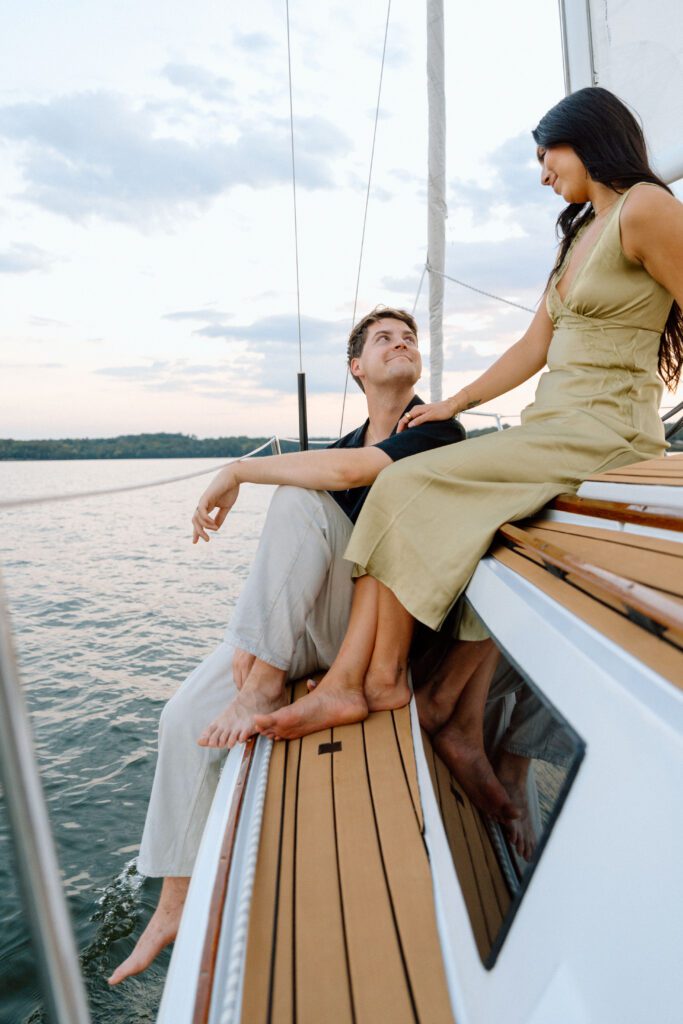 Couple sitting at the front of the sailboat during golden hour and smiling at each other