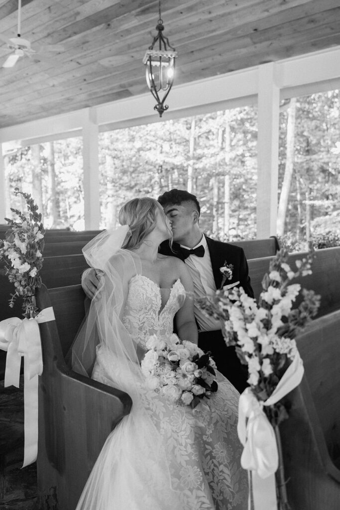 Bride and groom sitting in the pews of the chapel exchanging a kiss