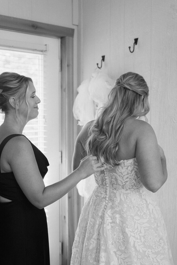 maid of honor zipping up the brides dress on her wedding day
