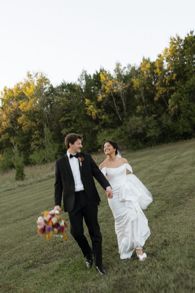 couple walking through the fields at drakewood farm and smiling on wedding day
