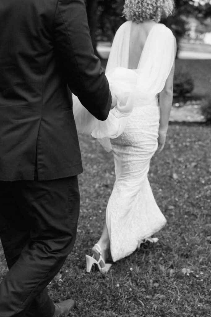 candid moment of groom holding brides dress while walking