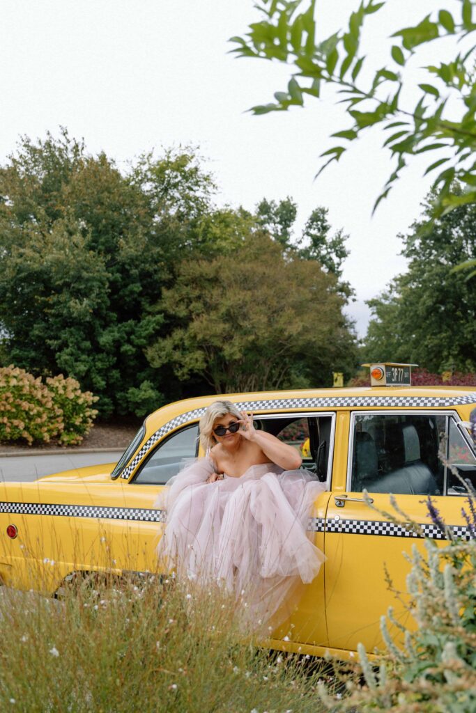 bride hanging outside the side of a vintage taxi at huntsville botanical garden wedding in the fall