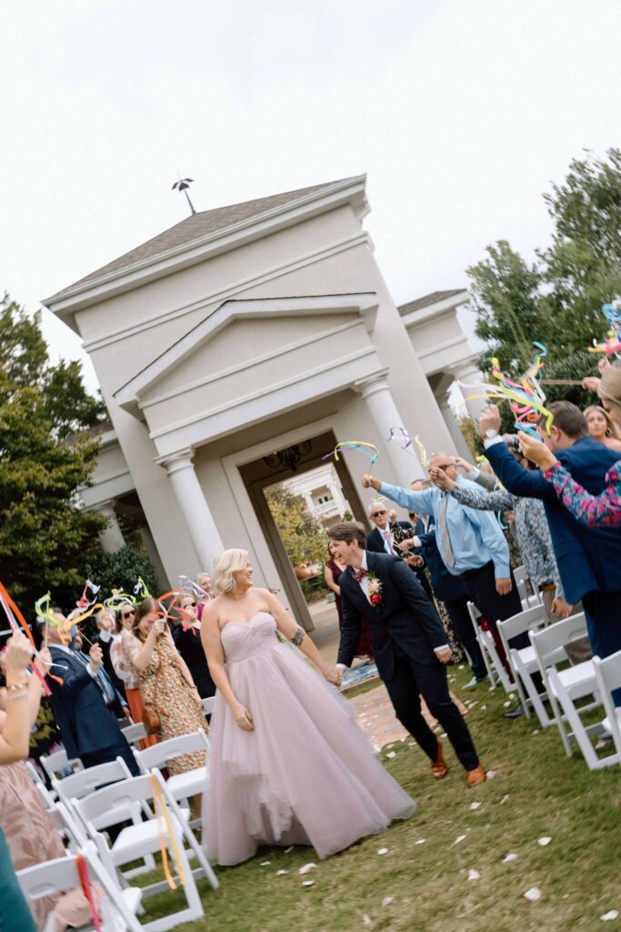 couple exiting their wedding ceremony while guests wave colorful ribbons around in the air