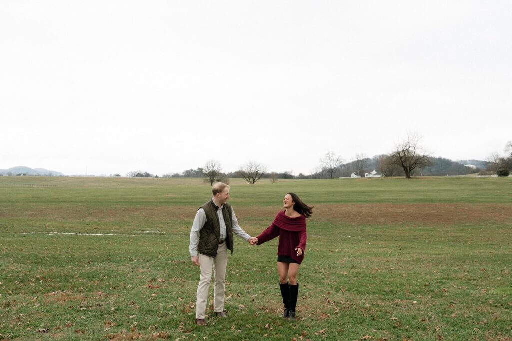 couple holding hands and laughing in a field after getting engaged