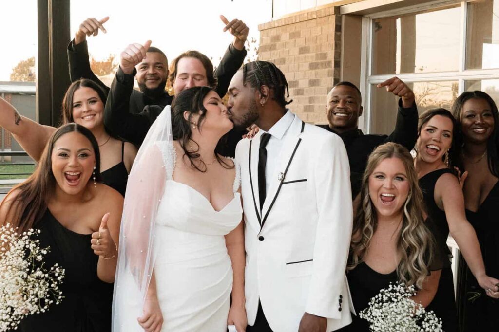 Bridal party cheering as bride and groom kiss on their wedding day