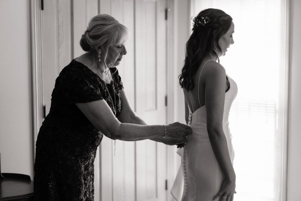 mother of the bride helping her zip up her dress on wedding day