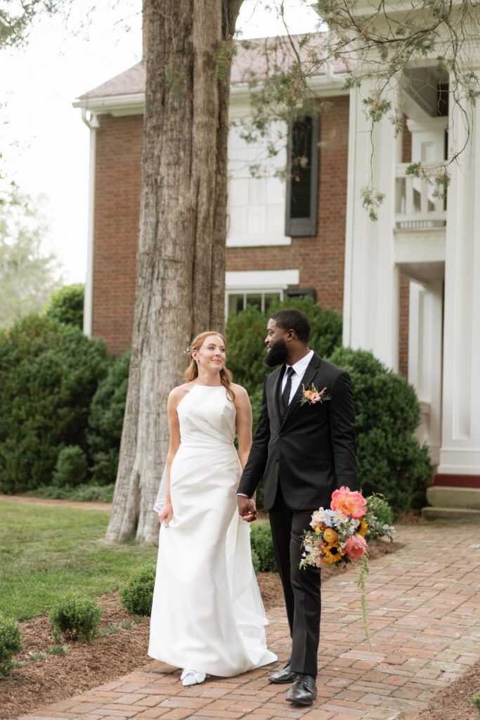 couple holding hands walking outside of historic house at cedarmont farm in franklin tennessee