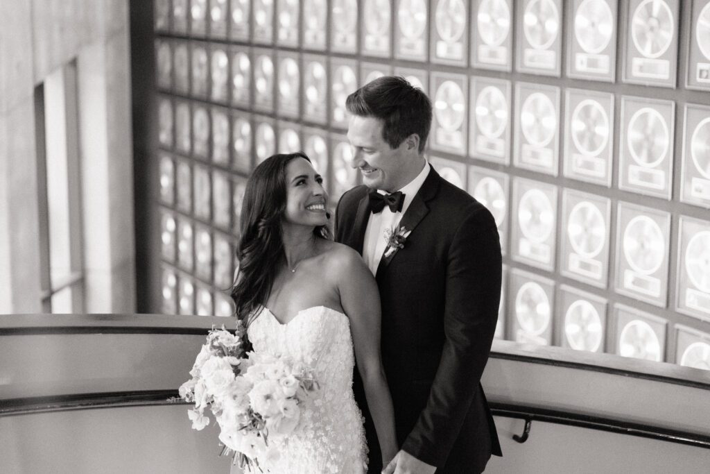 couple holding hands and smiling in front of the record wall at country music hall of fame wedding