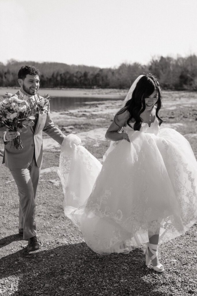 groom carrying bride's dress as they walk through the park in nashville