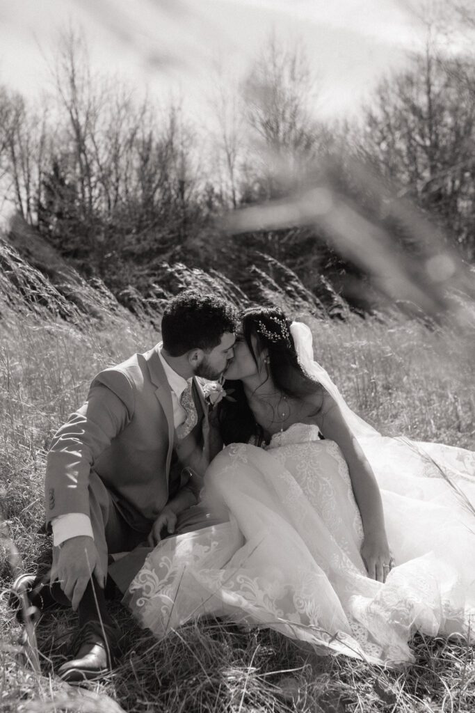 bride and groom sitting in the tall grass and kissing on their elopement day