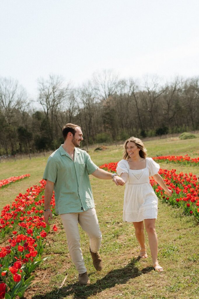 couple holding hands and walking through flower fields