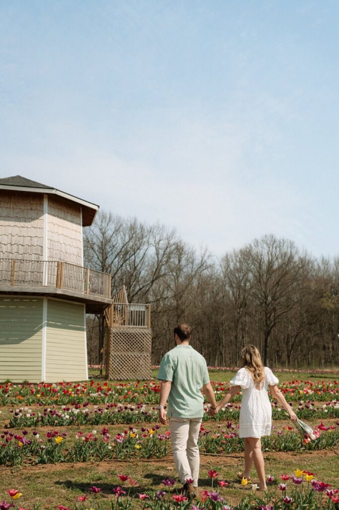 couple holding hands and walking through tulip farm during engagement session in nashville