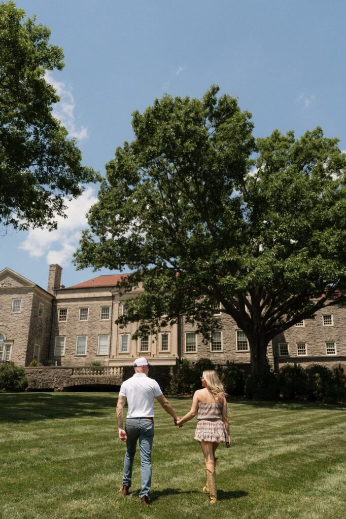 couple holding hands and walking along the lawn outside of cheekwood in nashville