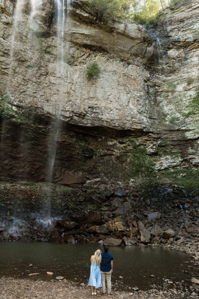couple staring up at the waterfall together during engagement session