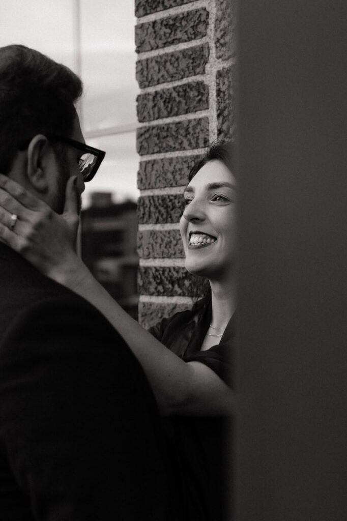 black and white photo of couple smiling against a brick wall