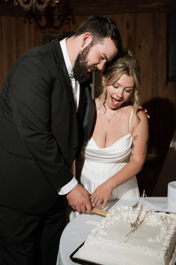 couple smiling while cutting their wedding cake