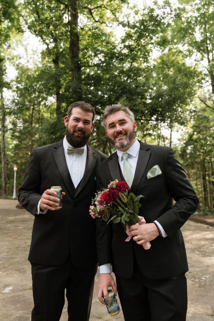 groom and best man posing for a photo with a beer and flowers at stone gate farm in nashville