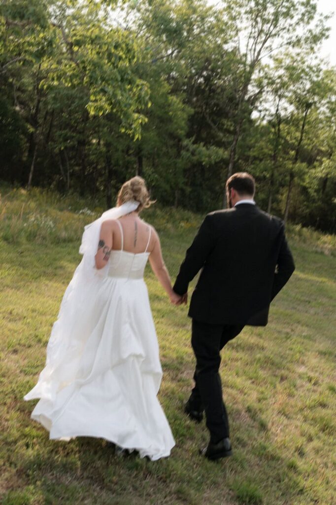 bride and groom holding hands and running through a field at stone gate farm wedding