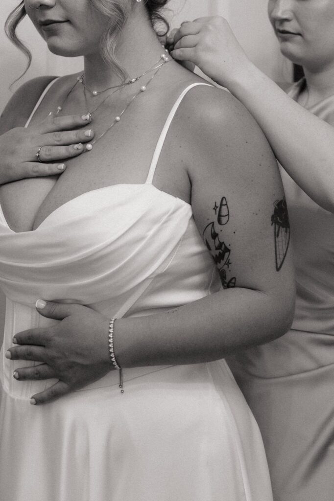 close up of bride putting on necklace with maid of honor