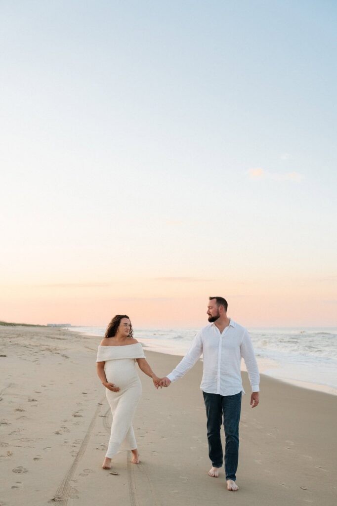 couple holding hands and walking on the beach in virginia beach