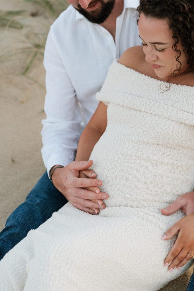 couple looking at pregnant belly during a sweet moment on the beach
