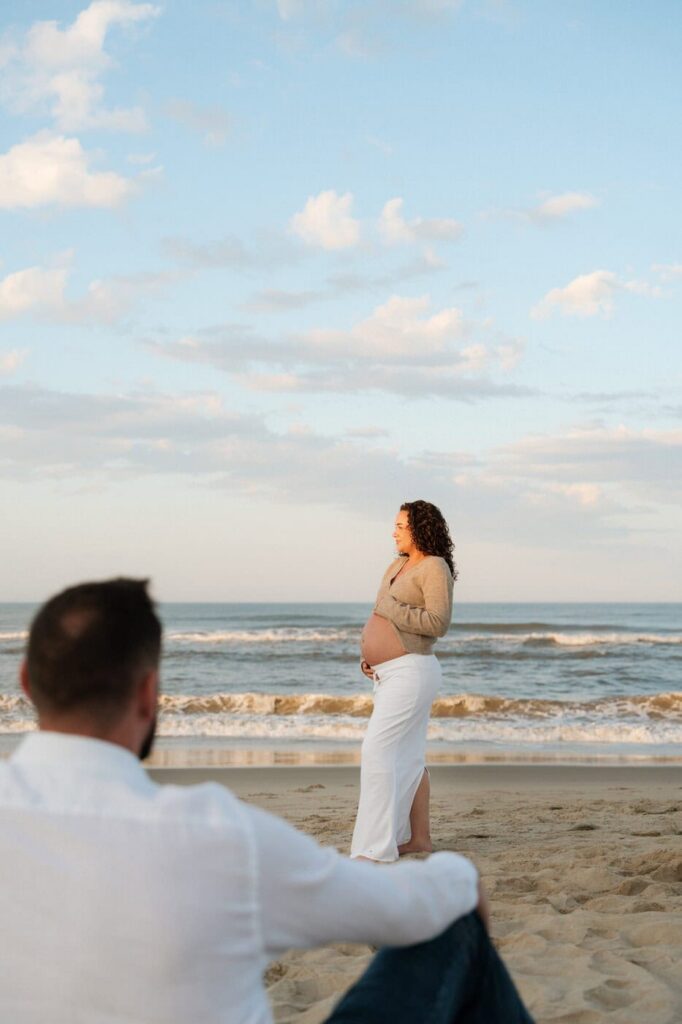 man looking at his pregnant wife during maternity session on the beach at sunset