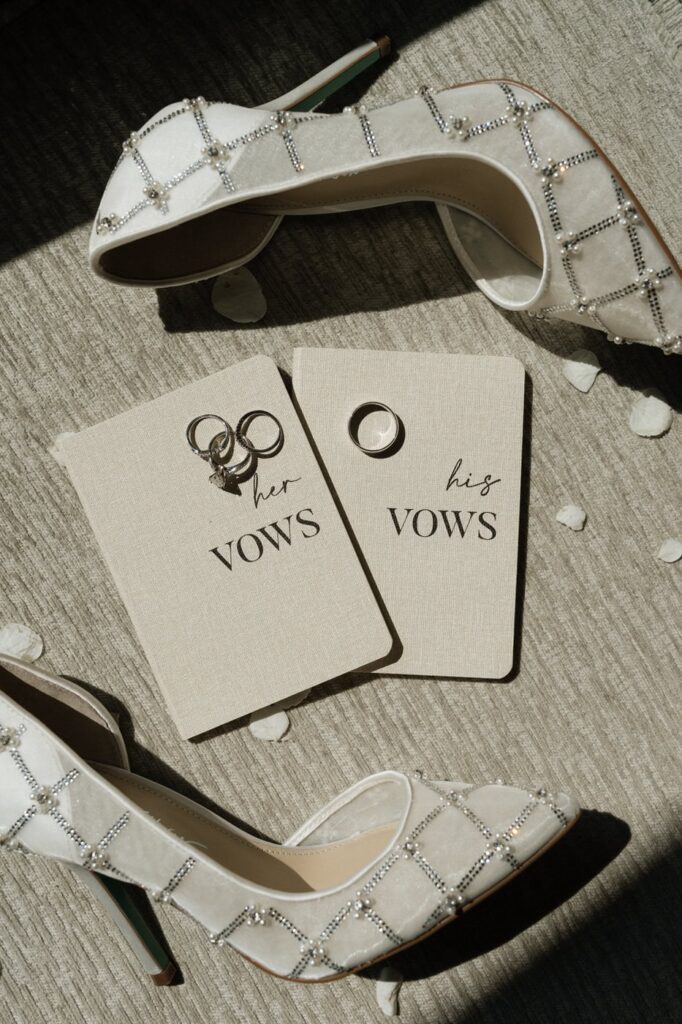 wedding detail shot of bridal shoes, vow books, rings, and loose florals